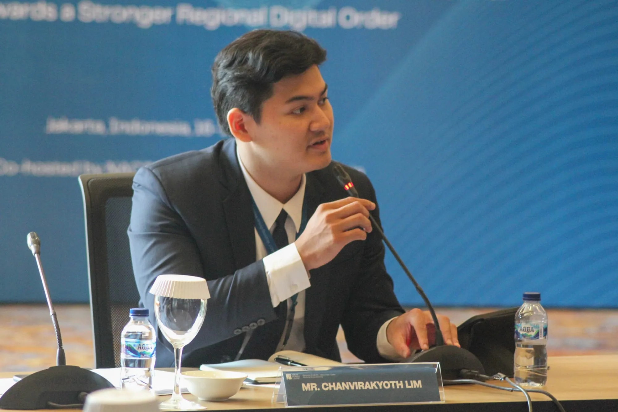 Lim Chanvirakyoth gesturing while speaking at the microphone, name plate in front