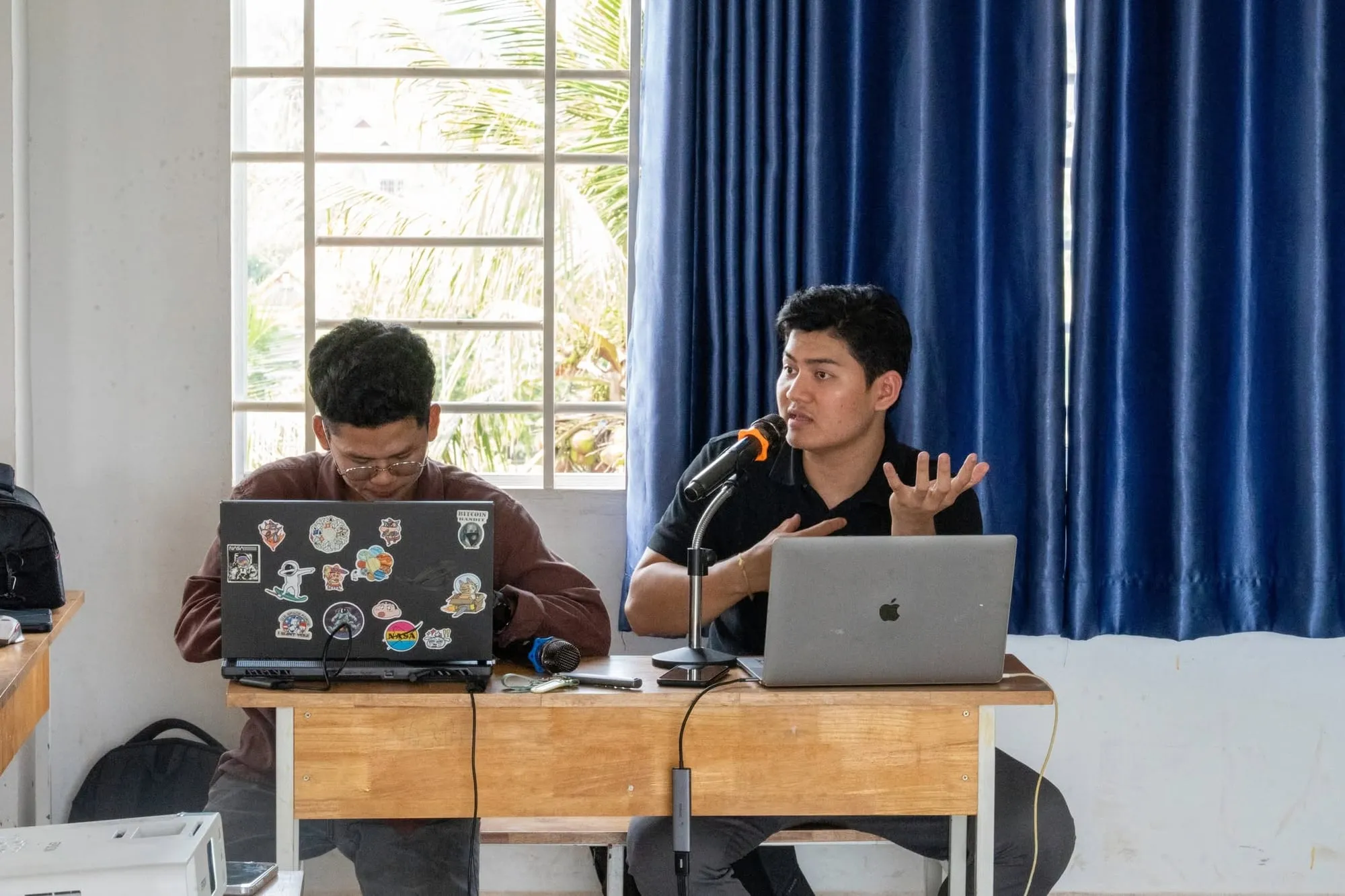 Lim Chanvirakyoth speaking into a microphone at a laptop beside a colleague